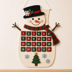 May include: A cream-colored crocheted snowman wall hanging featuring a black top hat with a white snowflake and red berries, a red and green striped scarf, and brown stick arms. It includes twenty-four numbered pockets and a green tree.