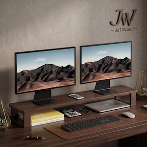 May include: A dark brown wooden monitor stand with a rectangular top and two side supports. The stand holds two computer monitors displaying mountain landscapes. The text JW JaTiWood is visible on the wall above the monitors.