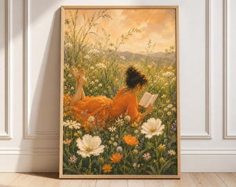 May include: A rectangular wall art print in a light wood frame depicting a person with dark hair in an orange dress lying in a field of white and orange wildflowers, reading an open book under a warm, golden-toned sunset sky with distant hills.