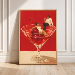 May include: A framed art print featuring a large martini glass filled with red liquid and a giant cherry. A person in a white swimsuit reclines inside the glass, while a person in a white tuxedo and black trousers sits on the rim holding a drink.