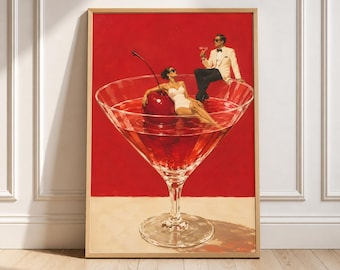 May include: A framed art print featuring a large martini glass filled with red liquid and a giant cherry. A person in a white swimsuit reclines inside the glass, while a person in a white tuxedo and black trousers sits on the rim holding a drink.