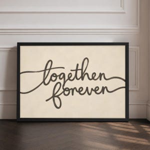 May include: A rectangular wall art print in a black frame featuring the words together forever written in a dark brown cursive script on a light beige background. The text is centred and spans across the middle of the off-white paper surface.