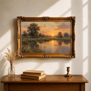 May include: A rectangular landscape painting in an ornate gold frame depicting a sunset over a calm pond surrounded by trees and grassy fields. The sky features soft orange and yellow hues reflecting on the water surface with dark green foliage.