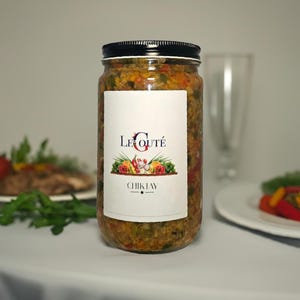 May include: A clear glass jar filled with a textured, multi-colored vegetable mixture. The jar has a black screw-top lid and a white label featuring the text LE GOUTÉ, a graphic of assorted vegetables, and the word CHIKTAY centered below.