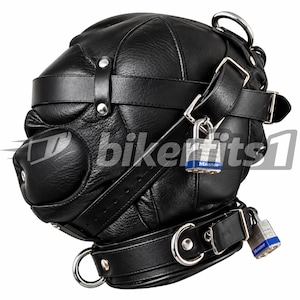 Könnte beinhalten: Eine schwarze Lederhaube mit mehreren verstellbaren Riemen, silberfarbenen Metallbeschlägen und zwei Master-Vorhängeschlössern mit blauen Akzenten. Die Haube verfügt über einen markanten schnauzenartigen Vorsprung und ein Halsband mit D-Ringen.