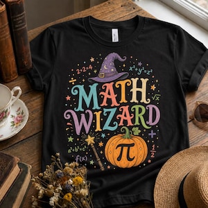 May include: A black t-shirt featuring a colourful graphic with the text MATH WIZARD, a purple witch hat, a pumpkin with a pi symbol, a magic wand, and various mathematical equations including 2+2=4, x²+y²=z², and f(x) scattered among small stars.
