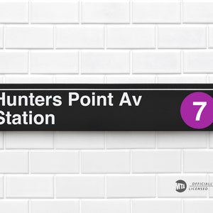 May include: Black and white sign with the text "Hunters Point Av Station" and a purple circle with the number "7" inside. The sign is on a white tiled wall with an MTA logo in the bottom right corner.