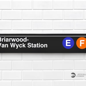 May include: A black and white sign with the text "Briarwood-Van Wyck Station" and the letters "E" and "F" in blue and orange circles. The sign is mounted on a white tiled wall.