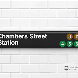 May include: Black and white sign with the text "Chambers Street Station" and subway line numbers and letters in colored circles: J, Z, 4, 5, 6. The sign is mounted on a white tiled wall.