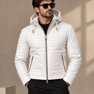 May include: A white hooded jacket featuring a textured, grid-like pattern across the surface. The jacket includes a full-length front zipper, two zippered side pockets, and adjustable drawstrings on the hood. It is worn over a black shirt.