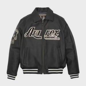 May include: A black leather bomber jacket featuring a full-length front zipper, a classic collar, and ribbed cuffs and hem with white stripes. The chest displays the white embroidered text 'Avirex' and 'BLACK ACES' with a graphic on the sleeve.
