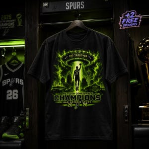 Peut inclure: Un t-shirt noir avec un motif vert néon représentant un joueur de basket soulevé par un OVNI au-dessus d'une ville. Le texte indique 210 TAKEOVER, WESTERN CONFERENCE CHAMPIONS, SAN ANTONIO SPURS, 20-26 et un petit logo des Spurs au centre.
