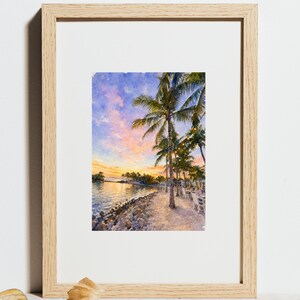 May include: A framed watercolour painting depicting a tropical beach scene at sunset. The artwork features tall palm trees, a sandy shoreline, and a vibrant sky with shades of pink, orange, and blue. String lights hang between the trees.