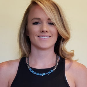 Puede incluir: Una mujer con el pelo largo y rubio lleva un top negro de tirantes y un collar con cuentas azules y plateadas.