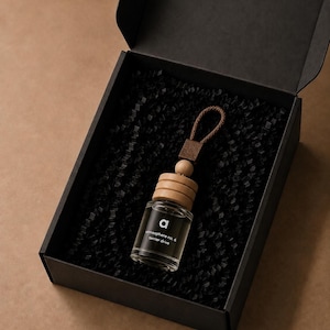 Può includere: Un piccolo flacone in vetro con tappo in legno e un cordino marrone, presentato in una scatola regalo nera riempita con carta nera sminuzzata. Il flacone presenta un'etichetta bianca con il testo 'a atmosphere no. 6 terrier drive' stampato.