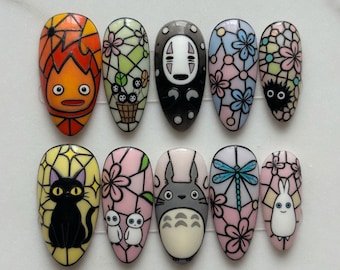 May include: A set of ten almond-shaped press-on nails featuring colorful stained glass-inspired designs. The artwork includes various animated characters, floral patterns, a black cat, a dragonfly, and soot sprites, all outlined in bold black lines.