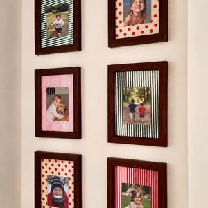 May include: Six rectangular dark brown wooden picture frames arranged in two columns on a wall. Each frame contains a photograph surrounded by a decorative mat featuring various patterns including red polka dots, green stripes, and red stripes.