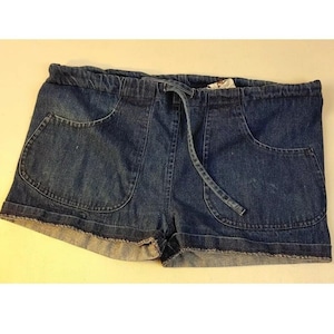 May include: Dark blue denim shorts featuring an elastic waistband with a matching drawstring tie. The shorts include two large rounded front pockets and have a raw, frayed hemline along the bottom edges, showcasing a classic medium wash finish.