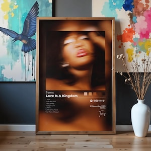 May include: A rectangular framed wall art print featuring a blurred portrait of a person with dark hair and red lips. The text reads Tems, Love Is A Kingdom, a tracklist of seven songs, the date 21 November 2025, 19 Min, and a signature.