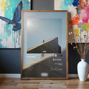 May include: A rectangular framed poster featuring the album cover for Daniel Caesar's Freudian. The artwork displays a person walking up a large concrete structure against a clear sky. It includes a tracklist, release date, and Spotify code.