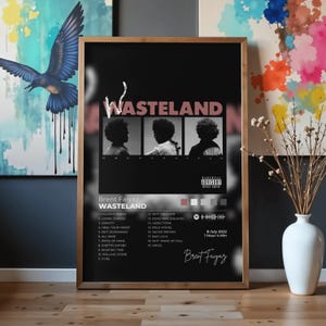 May include: A framed poster of the Brent Faiyaz album Wasteland with a black background, featuring three monochrome portraits, the title Wasteland in large pink letters, a tracklist of 19 songs, a parental advisory label, and a Spotify code.