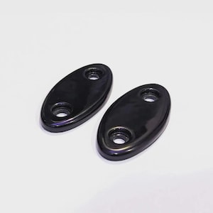 May include: Two identical oval-shaped black components with a smooth, glossy finish. Each piece features two circular holes positioned at opposite ends, designed for mounting or attachment purposes, presented against a plain white background.