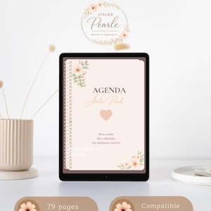 Peut inclure: Un agenda numérique à reliure spirale avec une couverture beige clair ornée d'illustrations florales, d'un cœur et du texte Agenda Atelier Pearle. L'écran affiche le texte Mon année, Mes objectifs, ma meilleure version et repousse tes limites.