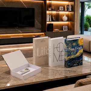 Può includere: Tre scatole decorative a forma di libro appoggiate su un tavolo in marmo. Una scatola è beige con la scritta Life, una è bianca con la scritta HOME e una raffigura La notte stellata di Van Gogh. Una scatola bianca aperta contiene un telecomando.