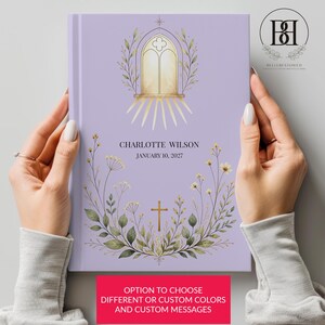 May include: A light purple hardcover book featuring a gold-colored illustration of a church window and a cross surrounded by botanical greenery. The text reads CHARLOTTE WILSON and JANUARY 10, 2027. A pink rectangular box contains the text OPTION TO CHOOSE DIFFERENT OR CUSTOM COLORS AND CUSTOM MESSAGES.
