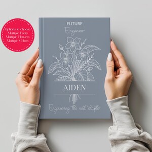 May include: A slate blue hardcover book featuring a white line-art floral illustration, the text "FUTURE Engineer", the name "AIDEN" centered in a box, and the phrase "Engineering the next chapter" printed in a script font at the bottom.