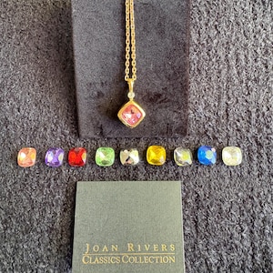 May include: A gold-tone necklace with a pink cushion-cut pendant, accompanied by nine interchangeable square-cut stones in various colors. A small card displays the text Joan Rivers Classics Collection in gold lettering on a dark background.