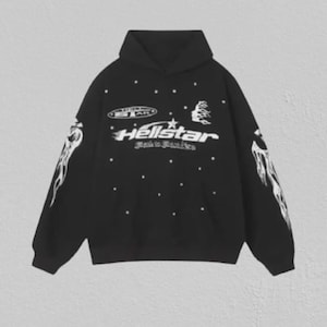 May include: A black long-sleeve hooded sweatshirt featuring white graphic prints on the front and sleeves. The front displays the text Hellstar with a star icon, smaller text below, and scattered white dots. Each sleeve features a white flame graphic.