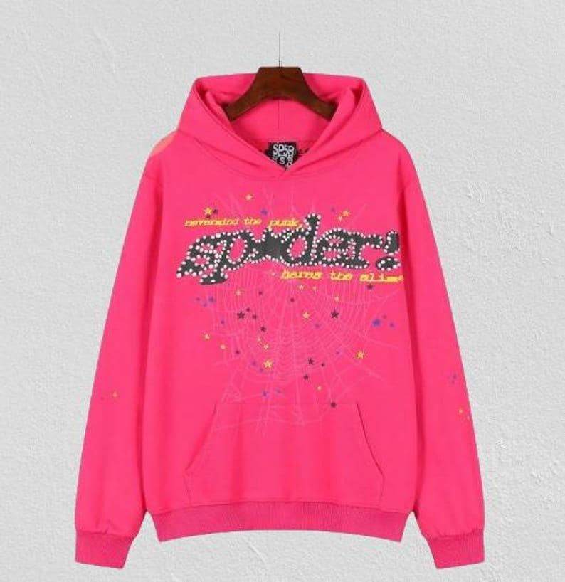 Op de afbeelding: Een felroze hoodie met lange mouwen en een grote afbeelding op de voorkant. De afbeelding toont het woord spider in een zwart gestippeld lettertype, omringd door een spinnenwebontwerp, kleurrijke sterren en de tekst nevermind the punk, heres the slime.