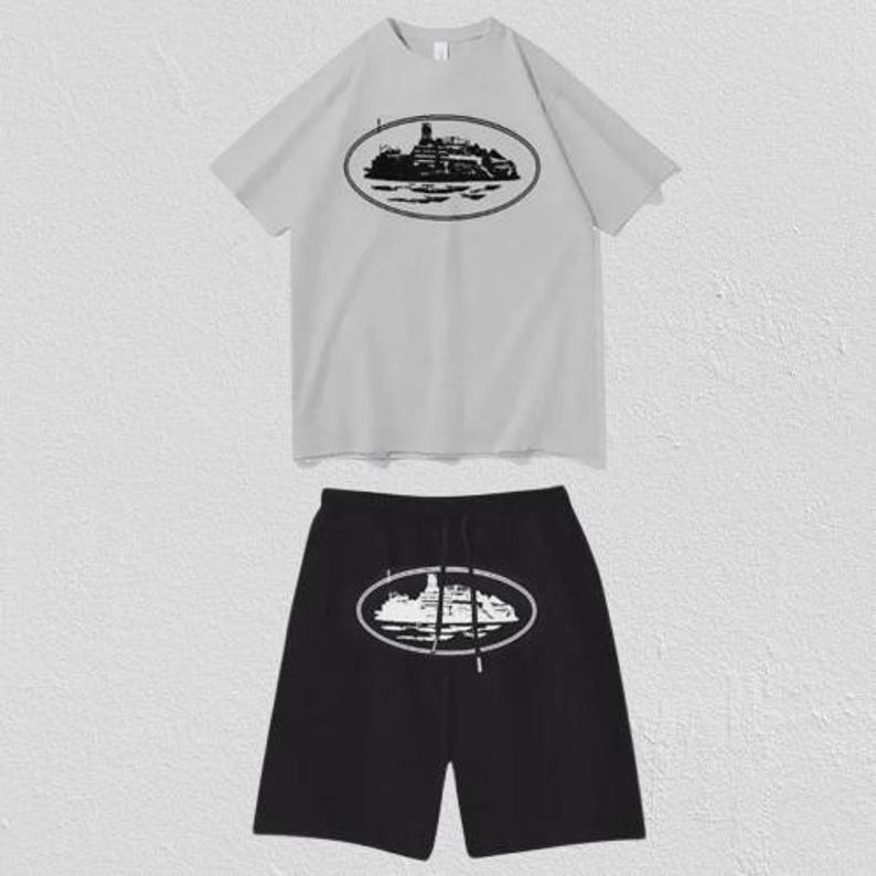 Puede incluir: Un conjunto de camiseta de manga corta gris claro y pantal&oacute;n corto negro. La camiseta presenta un gr&aacute;fico ovalado negro de un barco en el pecho. El pantal&oacute;n corto negro tiene un gr&aacute;fico ovalado blanco del mismo barco con cord&oacute;n en la cintura.