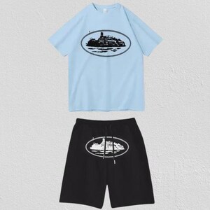 Puede incluir: Un conjunto de camiseta de manga corta azul claro y pantal&oacute;n corto negro. La camiseta presenta un gr&aacute;fico ovalado negro de un barco en el pecho. El pantal&oacute;n corto negro tiene un gr&aacute;fico ovalado blanco a juego en el centro y cord&oacute;n ajustable.