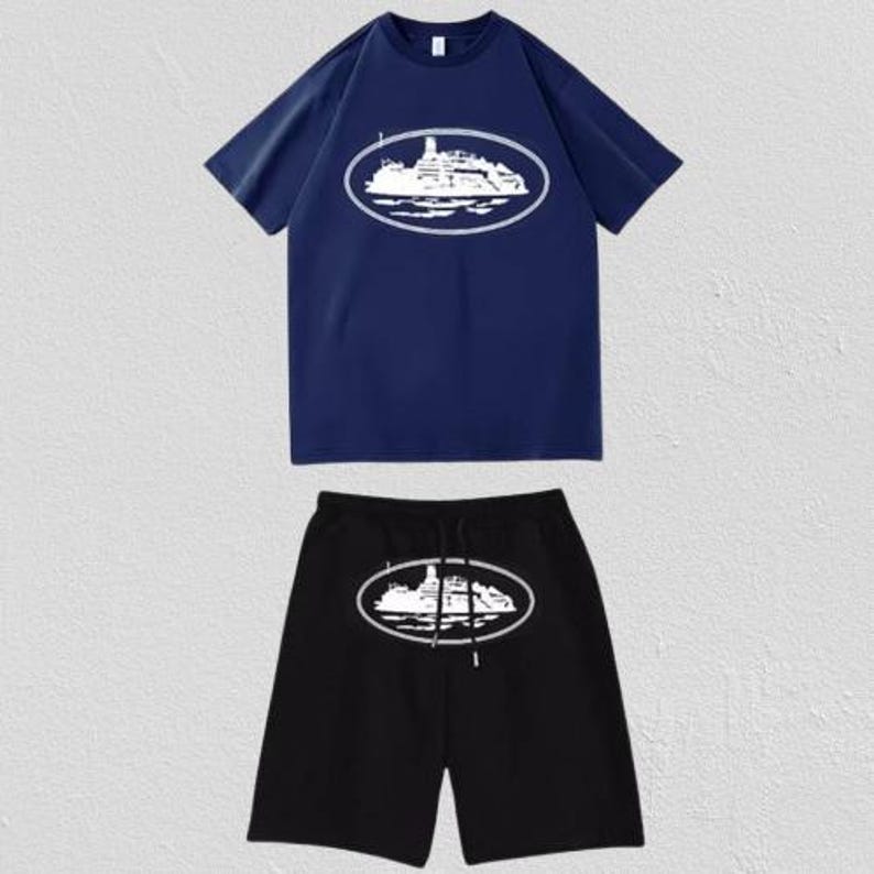 Puede incluir: Un conjunto de camiseta azul marino de manga corta y pantal&oacute;n corto negro. La camiseta presenta un gr&aacute;fico blanco de un barco dentro de un marco ovalado en el pecho. El pantal&oacute;n corto negro tiene un gr&aacute;fico de barco a juego y un cord&oacute;n negro.