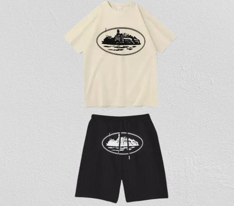 Puede incluir: Un conjunto de camiseta de manga corta color crema y pantalones cortos negros. La camiseta presenta un gr&aacute;fico ovalado negro de un barco en el pecho. Los pantalones cortos negros tienen un gr&aacute;fico ovalado blanco a juego en la pierna y cintura con cord&oacute;n.