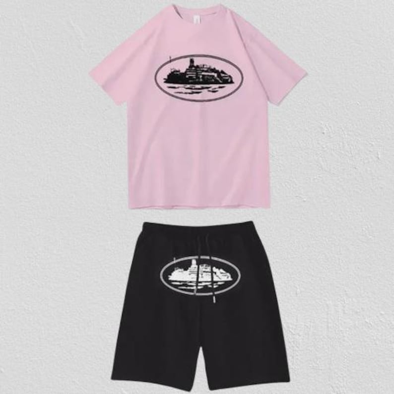 Puede incluir: Un conjunto de camiseta rosa claro de manga corta y pantal&oacute;n corto negro. La camiseta presenta un gr&aacute;fico ovalado negro de un barco en el pecho. El pantal&oacute;n corto negro muestra un gr&aacute;fico ovalado blanco del mismo barco y tiene un cord&oacute;n ajustable.