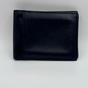 May include: A dark navy blue leather bifold wallet featuring a smooth, matte finish and clean, straight stitching along the edges. The wallet has a rectangular shape with a vertical panel detail on the left side and a plain, solid front surface.