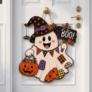 May include: A hanging Halloween door sign shaped like a white ghost wearing a black polka-dot witch hat. The ghost holds a jack-o'-lantern bucket filled with sweets and a sign that says BOO. It features colourful patches and a small spider.