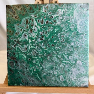 May include: A square canvas featuring an abstract acrylic pour painting with swirling patterns of emerald green, white, silver, and dark brown. The paint creates a marbled effect with distinct cells and fluid lines across the textured surface.