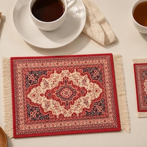 May include: A rectangular placemat and a smaller square coaster, both featuring a red, cream, and dark blue intricate woven pattern with fringe on the short ends. The designs mimic the appearance of a traditional rug with a central medallion.