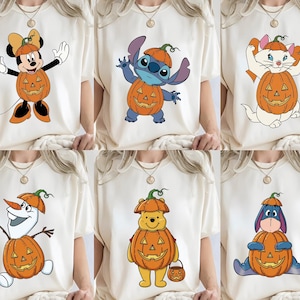 May include: A collection of six off-white t-shirts, each featuring a different cartoon character wearing a carved orange pumpkin costume. The characters include Minnie Mouse, Stitch, Marie the cat, Olaf, Winnie the Pooh, and Eeyore, all in festive attire.
