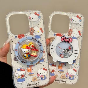 May include: Two clear phone cases featuring a repeating Hello Kitty pattern with small glitter accents. One case has a circular grip with a Hello Kitty figure, while the other features a white Hello Kitty-shaped clock grip with a pink bow.