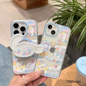 May include: Two clear phone cases featuring Cinnamoroll character graphics, pastel stars, moons, and clouds. One case includes a large, translucent, shaped Cinnamoroll phone grip with internal floating glitter elements and the word Dream.