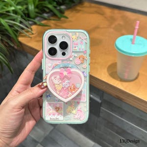 May include: A clear phone case with a light blue border featuring various cartoon animal stickers and a heart-shaped shaker attachment containing small colorful charms and a pink bow. The case has a pink camera lens frame and the text bunnies.