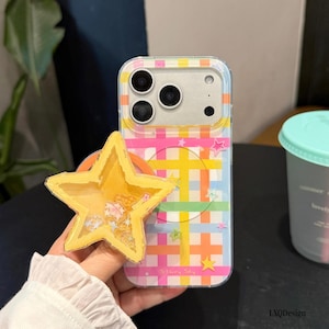 May include: A clear smartphone case featuring a colorful plaid pattern of yellow, orange, pink, and blue lines. A yellow star-shaped shaker attachment is affixed to the back, containing small loose star-shaped sequins. The text Starry Sky is printed.