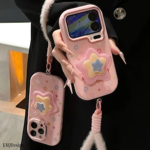 Capa para iPhone rosa pastel com estrelas em camadas, suporte Pop Socket 3D em formato de estrela e alça de pulso macia e fofa. Capa resistente a impactos para iPhone 17/16/15/14/13 Pro Max.