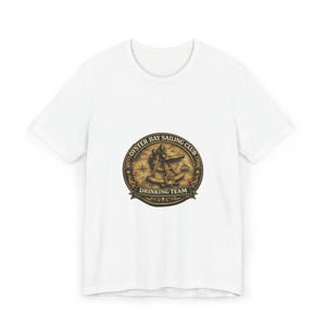 Pode incluir: Uma t-shirt branca de manga curta com um gráfico circular castanho no peito. O design inclui um sextante náutico, uma rosa dos ventos e um veleiro, com o texto OYSTER BAY SAILING CLUB DRINKING TEAM impresso em letras escuras.