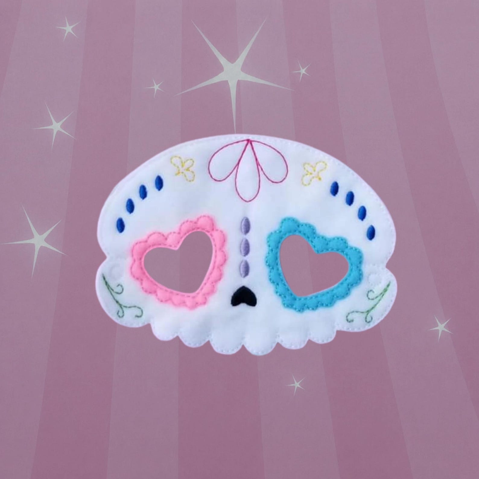 White decorative felt skull mask with pink and blue heart-shaped details.